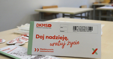 Zdjęcie przedstawia ulotki i inne gadżety Fundacji DKMS położone na ławce szkolnej.